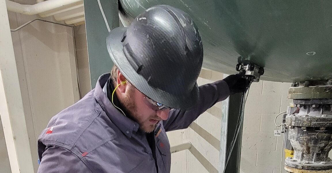 NDT technicians in hard hats and coveralls inspecting process piping